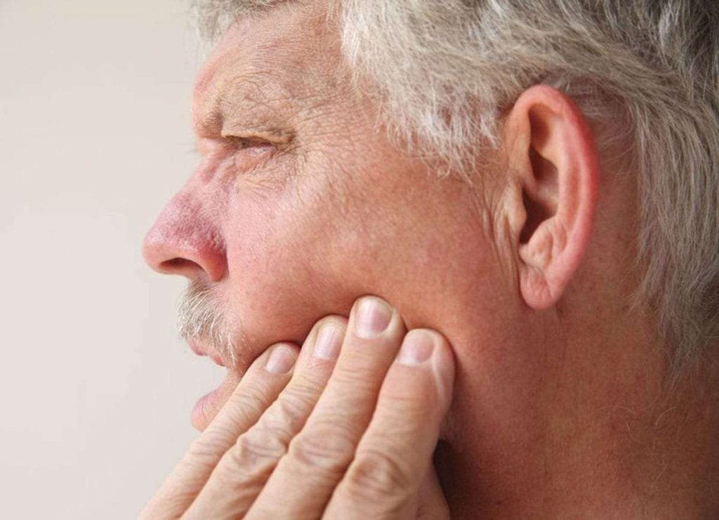 Person experiencing face pain, holding their cheek.